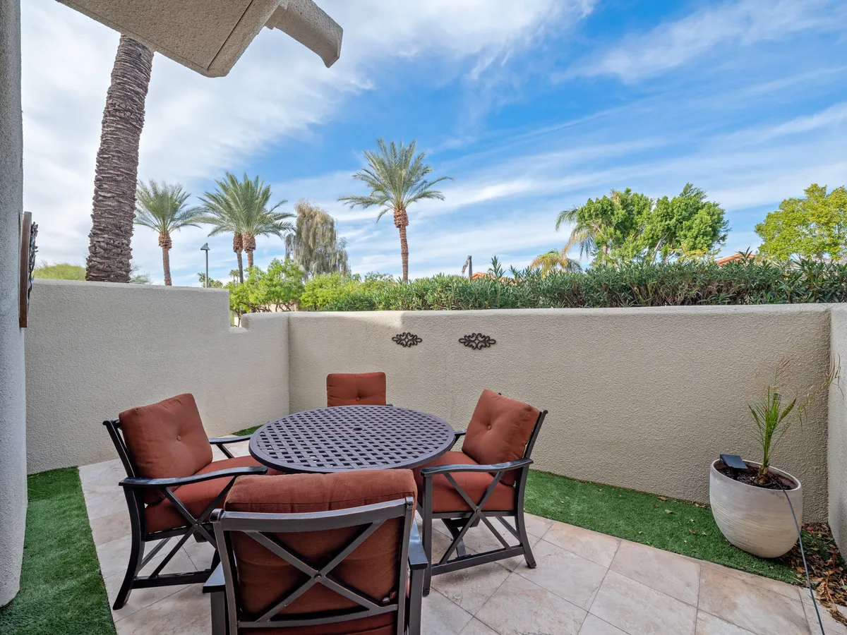 An exterior patio scene featuring a round table and four chairs nestled among palm trees and lush greenery. The inviting outdoor space blends relaxation with opportunities for social gatherings or post-workout unwinding.