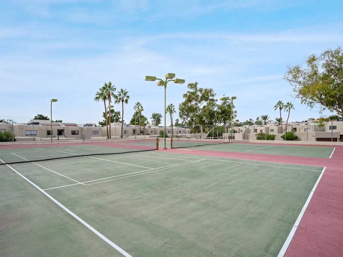 Energetic tennis courts framed by lush palm trees and residential buildings, suggesting an active and communal environment. The courts are well-maintained, emphasizing opportunities for group activities and exercise.