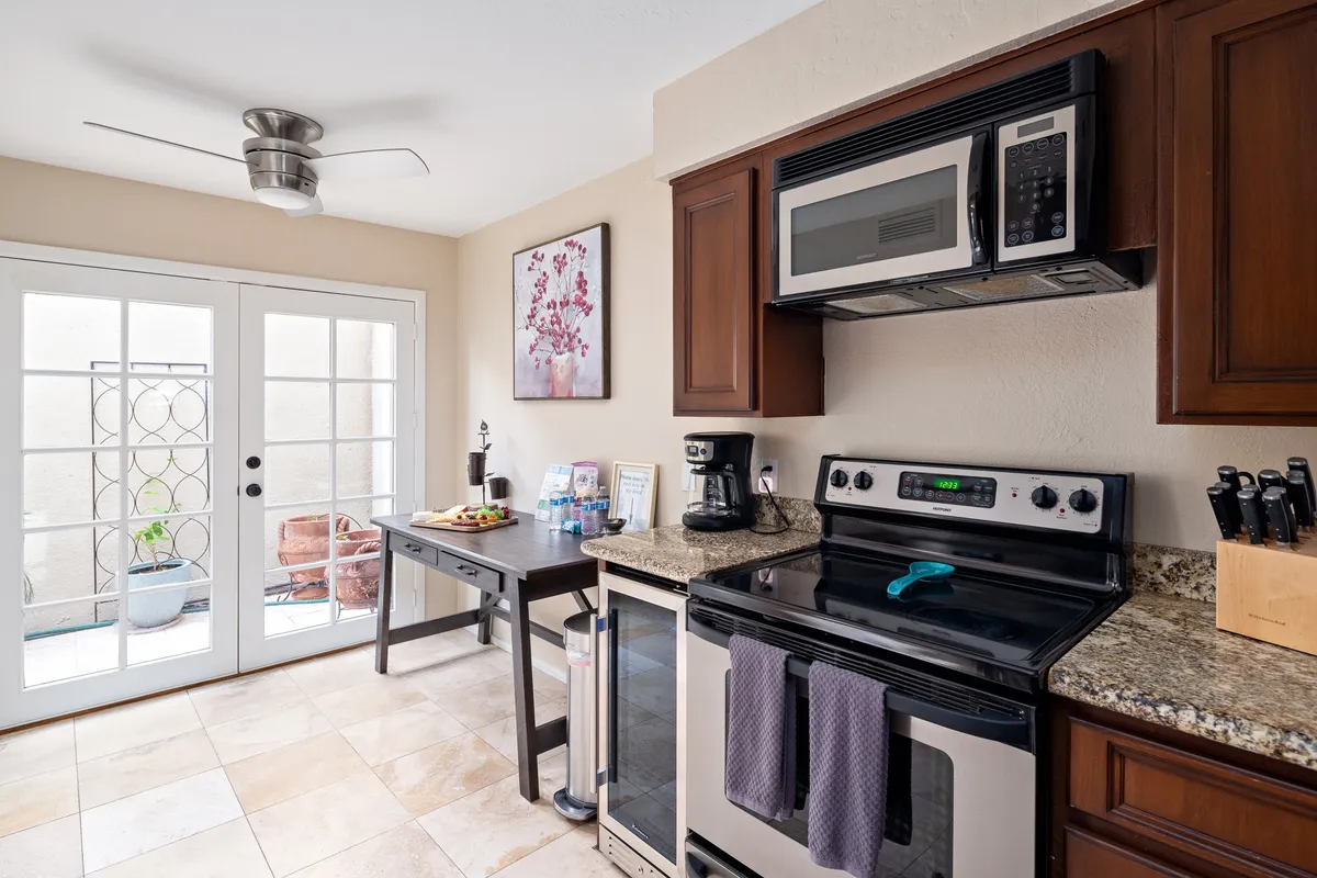 A bright, welcoming kitchen and dining area featuring stainless steel appliances, granite countertop, and a dining table set with refreshments. Artwork on the wall and natural lighting enhance the friendly, communal ambiance, making it perfect for casual gatherings or morning coffee at the breakfast bar.