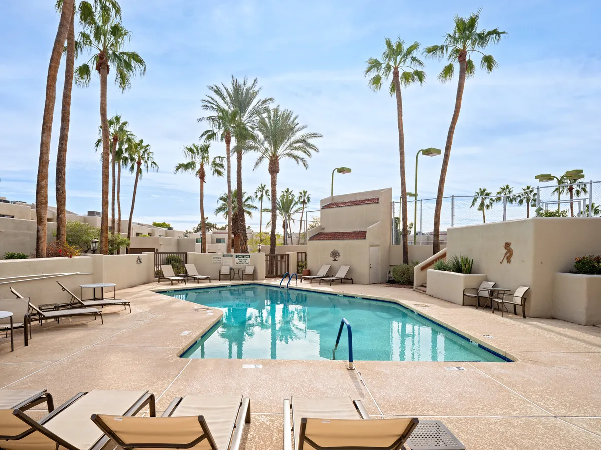 The image showcases a sparkling swimming pool surrounded by tall palm trees and inviting lounge chairs in the exclusive Biltmore Courts community. The scene exudes a tranquil, vacation-like atmosphere perfect for relaxation, sunbathing, and social gatherings, all set against the vibrant backdrop of Phoenix.