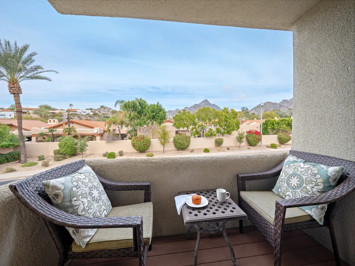 A serene seating area with comfortable chairs and a small table set with coffee and a pastry, all positioned to maximize a stunning mountain view. The atmosphere is peaceful and rejuvenating, perfect for morning reflection or winding down after activity.